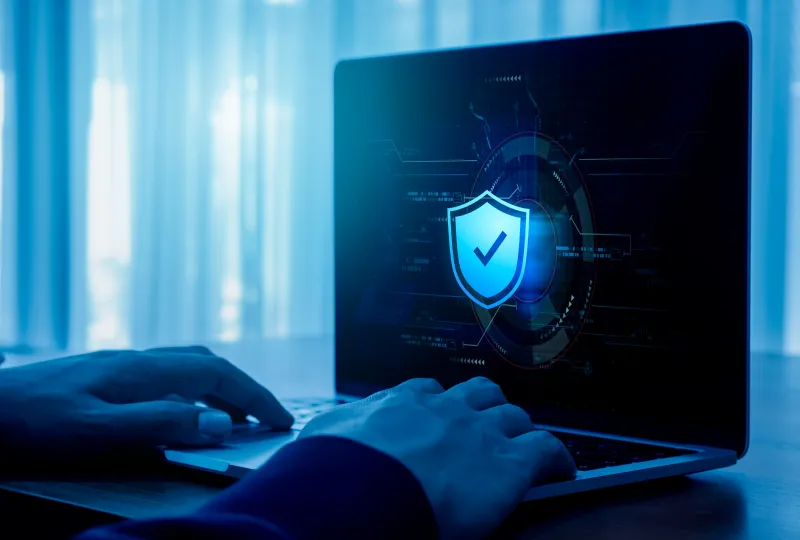 A person using their laptop with a blue shield on the screen.